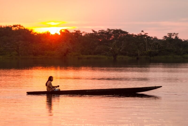 A man boats across a river in a dugout canoe, in the Cuyabeno Reserve of the Ecuadorian Amazon