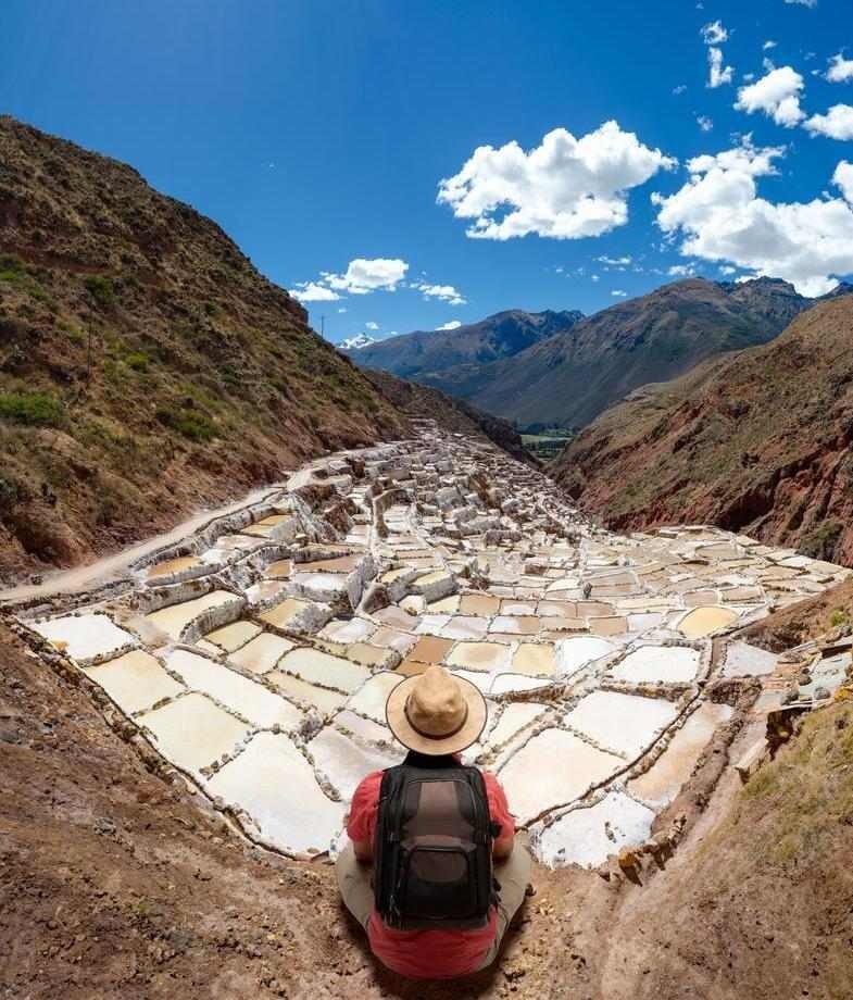 A hiker sitting on a rock facing the salt terraces of Maras in Cusco, Peru