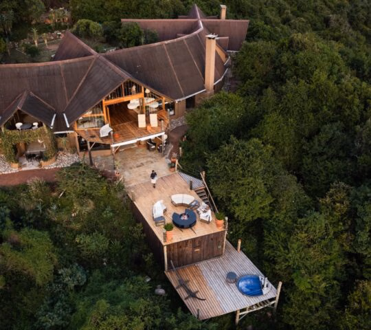 Aerial view of Cottar's Bush Villa, a multi-level lodge with a brown roof and tiered wooden decks amid lush forest.