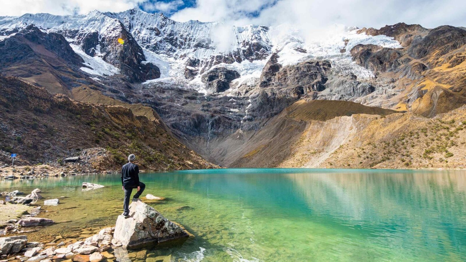 A hiker stands at the edge of Lake Humantay in Peru admiring the view