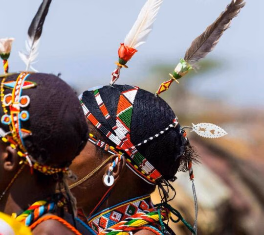 Close-up of people wearing traditional colourful beaded headbands and feathers on their hair.