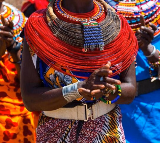 Close-up of vibrant red multi-strand beaded necklaces and traditional clothing worn outdoors.