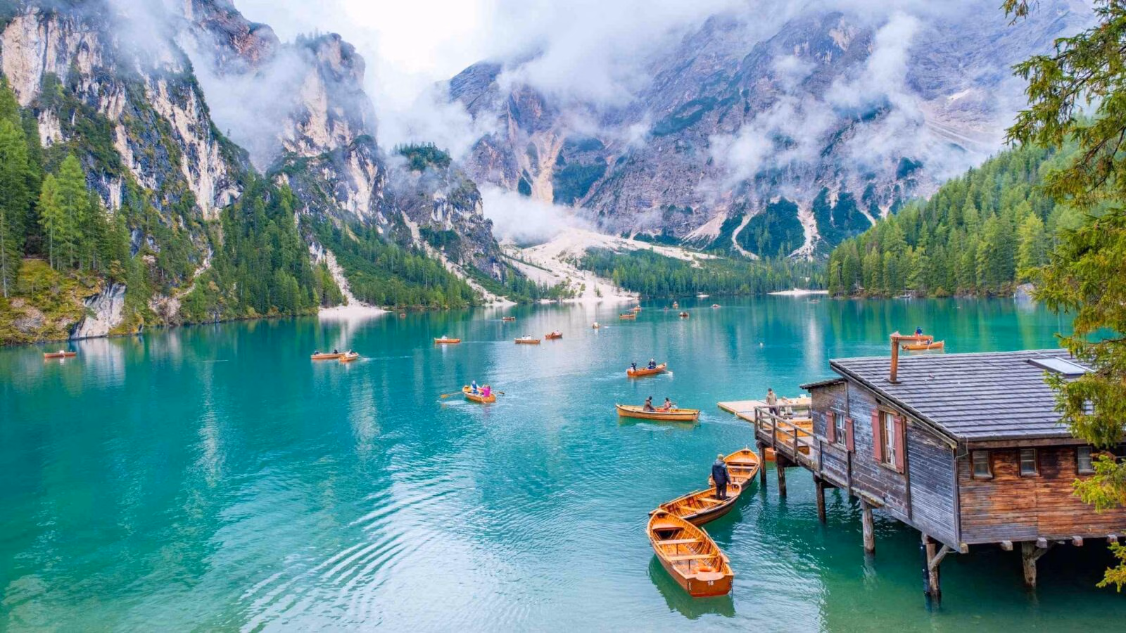 Small boats floating on a turquoise lake surrounded by mountains in the Dolomites