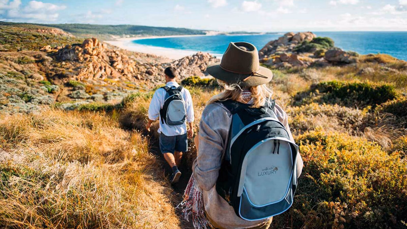 Two people hiking a coastal trail in Australia. One wears a backpack reading walk into LUXURY.