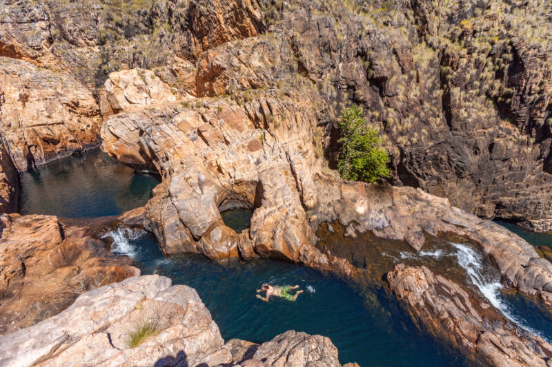A person swimming in a natural rock pool surrounded by rocky cliffs in Australia.