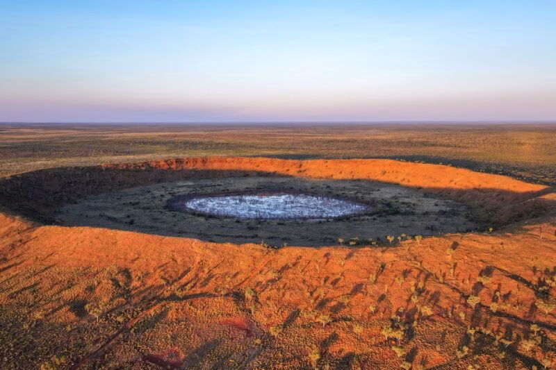Aerial view of a massive circular meteorite crater with a white center in the arid landscape of Australia.