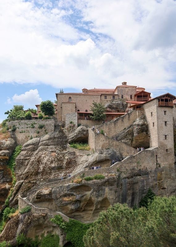 Ancient stone monasteries built on top of towering rock formations in Meteora, Greece, with a winding staircase for visitors.