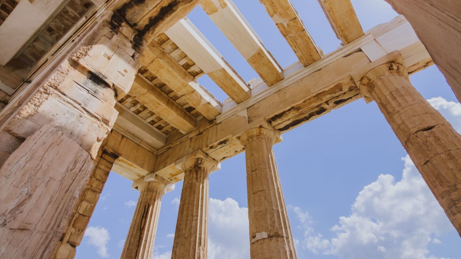 Low angle view looking up at the ancient stone Doric columns and roof beams of the Parthenon in Athens, Greece.