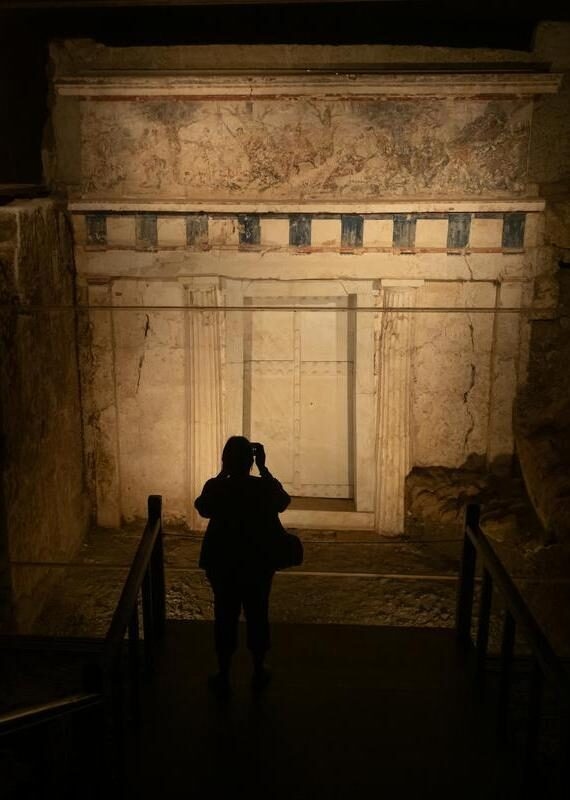 Silhouette of a person taking a photo of the Royal Tombs of Aigai in Greece, showing a large stone door and painted frieze.