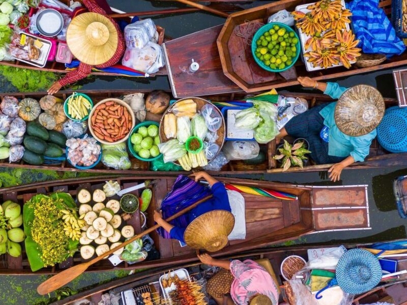 Overhead view of narrow wooden boats filled with fresh produce, rowed by people wearing traditional conical hats.