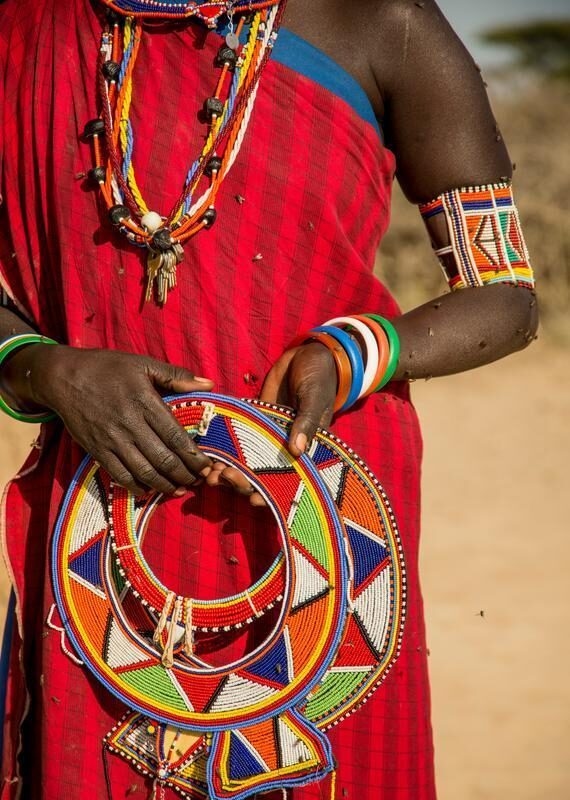 Person in red clothing holding a large circular beaded collar, wearing beaded necklaces and bracelets.