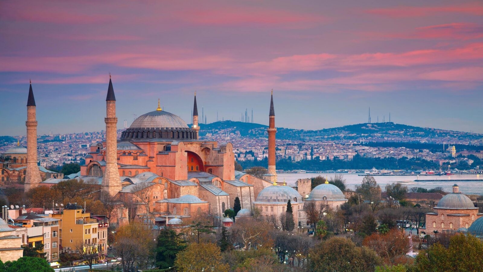 Hagia Sophia in Istanbul at sunset, featuring a large central dome and four minarets against a pink and purple sky.