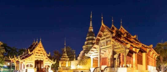 Illuminated Buddhist temple complex with golden spires and ornate pavilions under a dark starry sky at night.