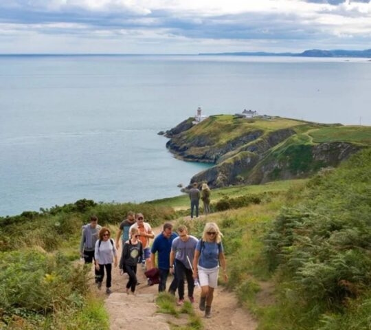 A group of people walking up a cliff at Howth Head in Dublin, Ireland with the sea in the background