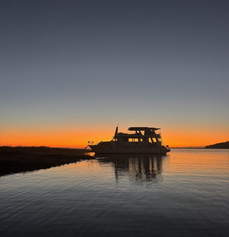 A houseboat silhouetted against a bright orange sunset on the water at lake kariba zimbabwe.