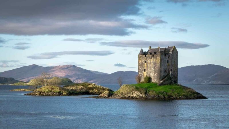 Historic stone castle building on a small island surrounded by calm water and distant mountains.