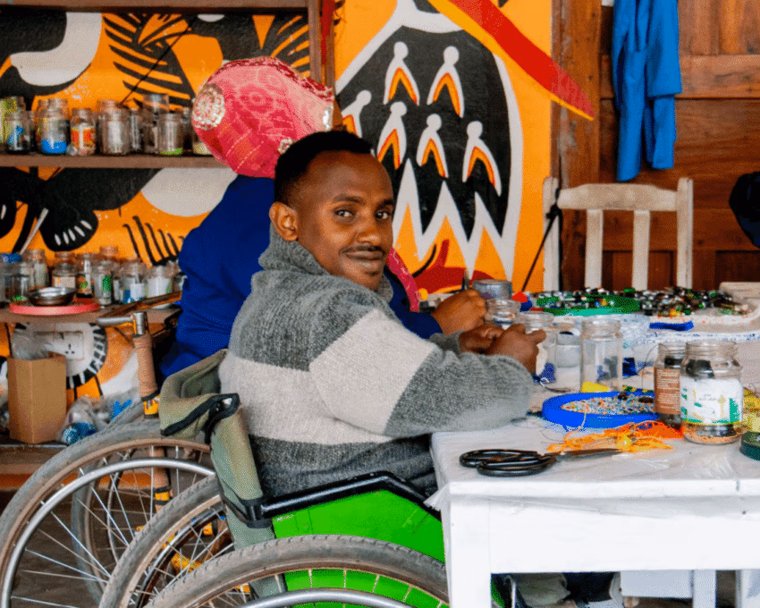 An artist in a wheelchair making jewellery from beads at the Shanga experience in Arusha