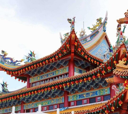 Close-up of a multi-tiered Chinese temple roof decorated with colorful dragon figures and hanging red lanterns.