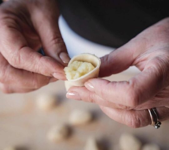 Close-up of two hands folding fresh pasta dough around filling.
