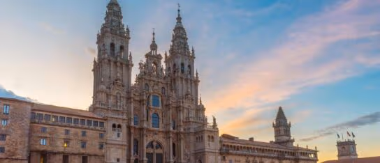 Ornate stone cathedral with two tall spires and detailed carving stands illuminated at sunset under a soft sky.