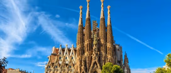Tall stone spires of the Sagrada Familia church against a bright blue sky with wispy clouds.