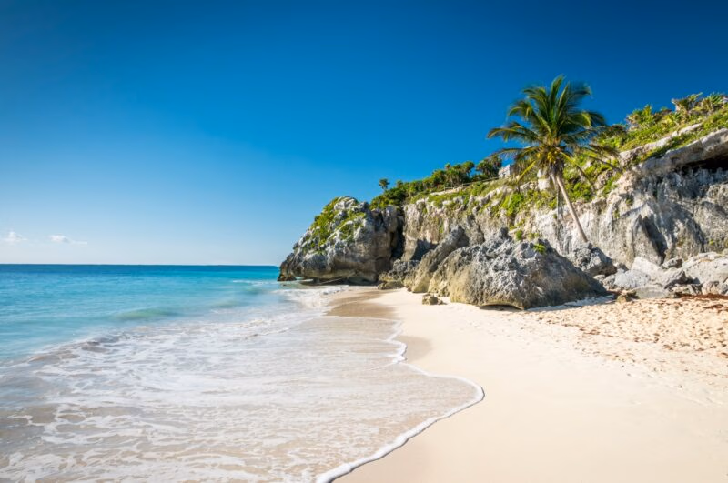 Turquoise waves crash against the white sand beach at the Tulum ruins in Mexico.