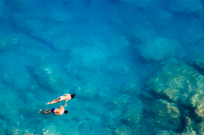 Aerial view of two people snorkeling in clear turquoise water on luxury Honeymoons.