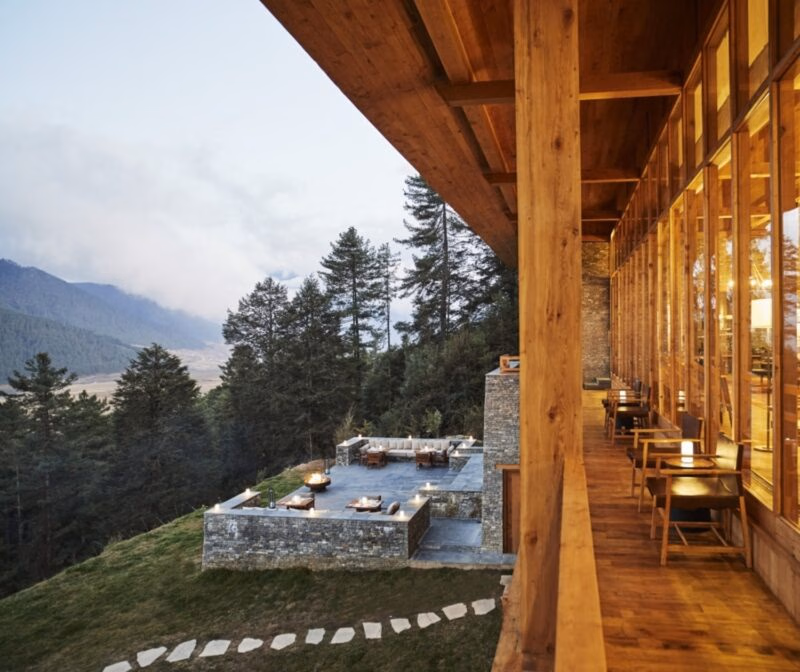 A wooden balcony at Six Senses Gangtey overlooks a stone patio and a mountain valley.