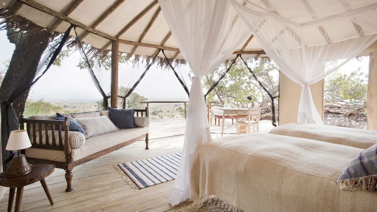 Interior of bedroom at Lamai Serengeti, twin beds with mosquito nets and sofa, open sides with view of the Serengeti National Park, Tanzania