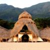 Exterior of Greystoke Mahale constructed of recycled dhows and thatched palm leaf roof set in front of the Mahale Mountains, Tanzania