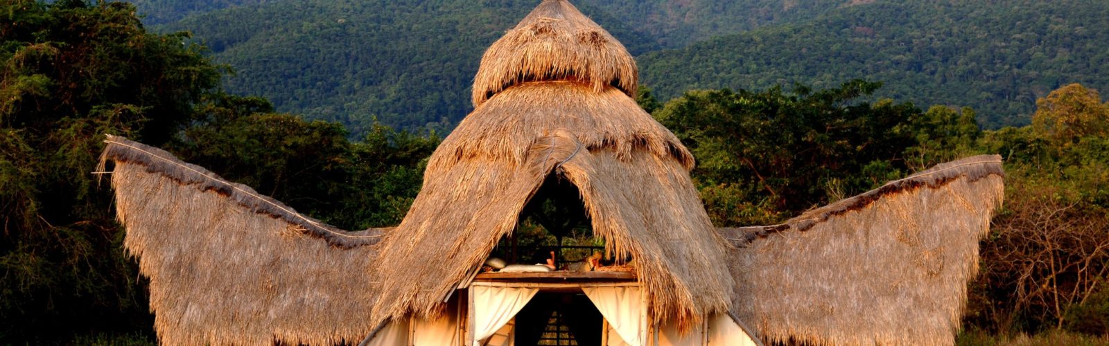Exterior of Greystoke Mahale constructed of recycled dhows and thatched palm leaf roof set in front of the Mahale Mountains, Tanzania