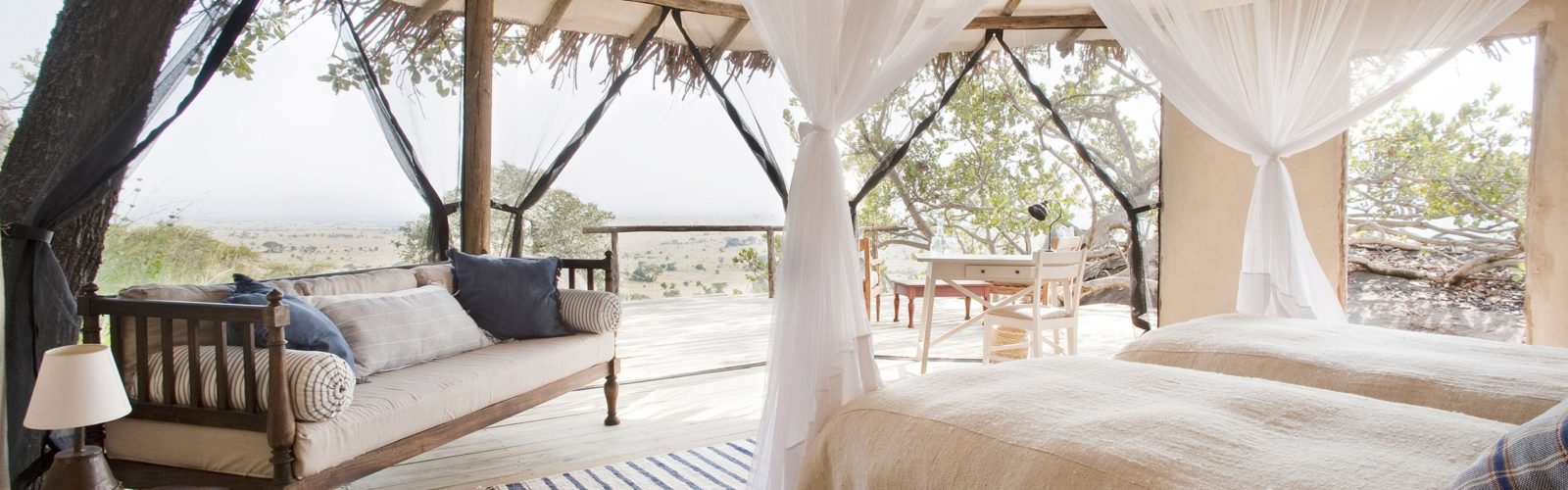 Interior of bedroom at Lamai Serengeti, twin beds with mosquito nets and sofa, open sides with view of the Serengeti National Park, Tanzania