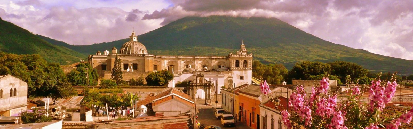 Aerial view of the city of Antigua in Guatemala, framed by pink spring flowers and dramatic mountains