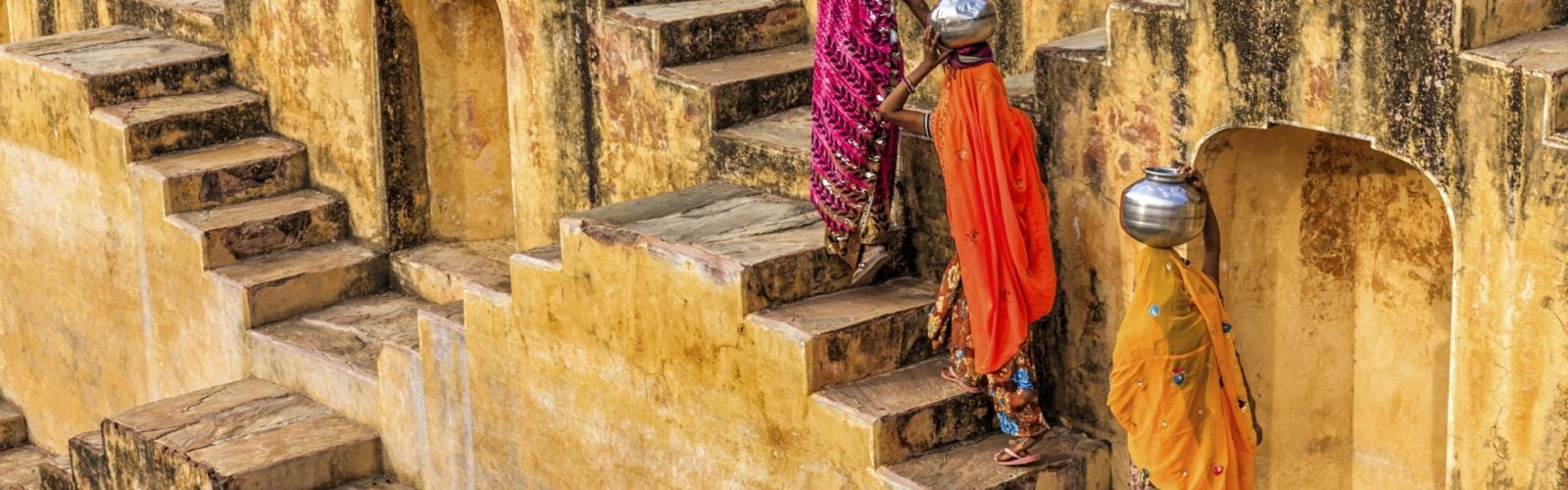 Three women in brightly coloured saris carrying water up the steps of a stepwell