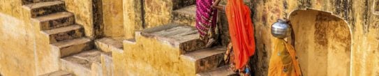 Three women in brightly coloured saris carrying water up the steps of a stepwell