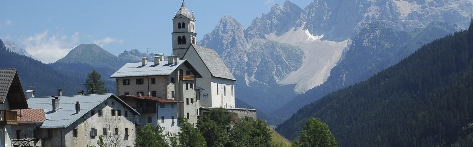 Colle Santa Lucia nestled in the lush green forests with the snow-capped Dolomites in the background, Belluno Italy