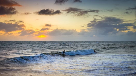 surfers-riding-waves-sunset
