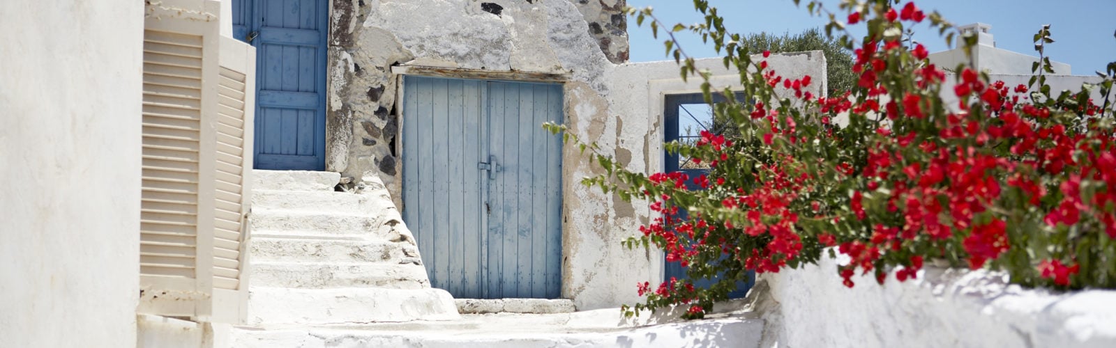 Red bouganvellia set against whitewashed stone building with blue wooden doors