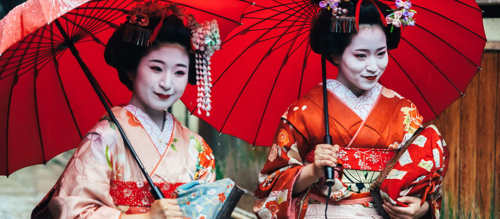Two maiko geisha walking on a street in Kyoto with red umbrellas