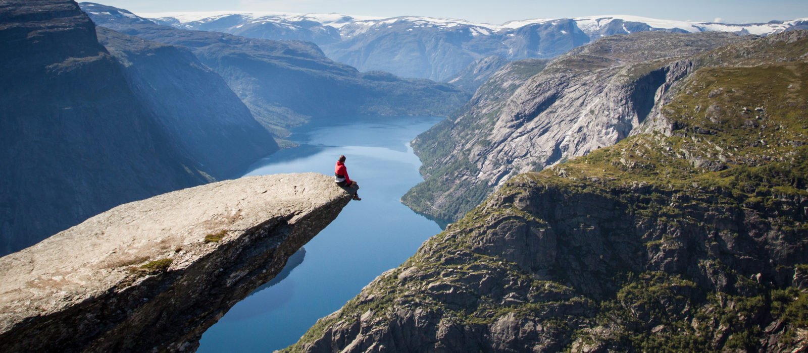 Tourist sitting on Trolltunga Rock above a Norwegian fjord