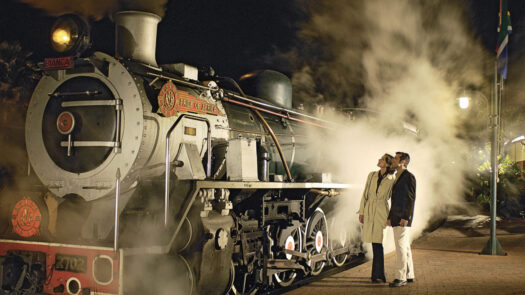 A couple stands beside a Rovos Rail train in Pretoria, South Africa.