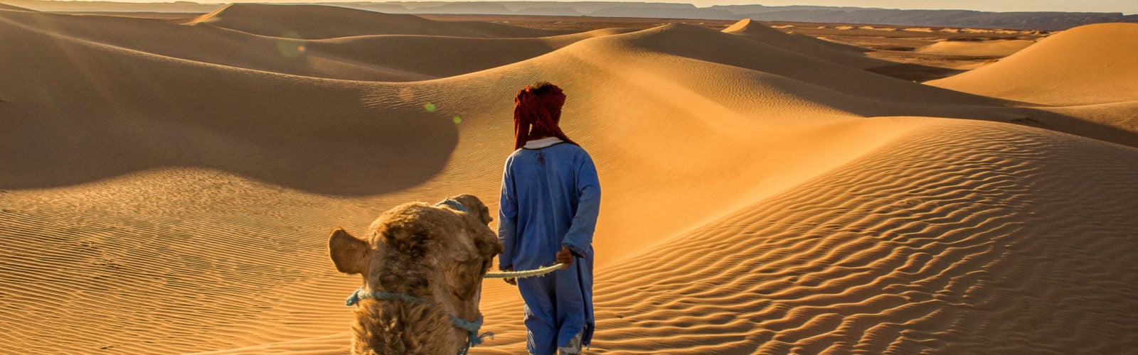 Berber walking through the dune landscape of the Sahara Desert in Morocco at golden hour