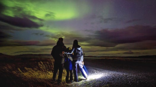 A family watches the northern lights in the night sky in Iceland.