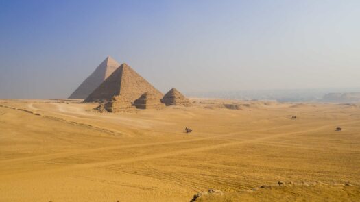 The pyramids of Egypt in the distance surrounded by desert sand.