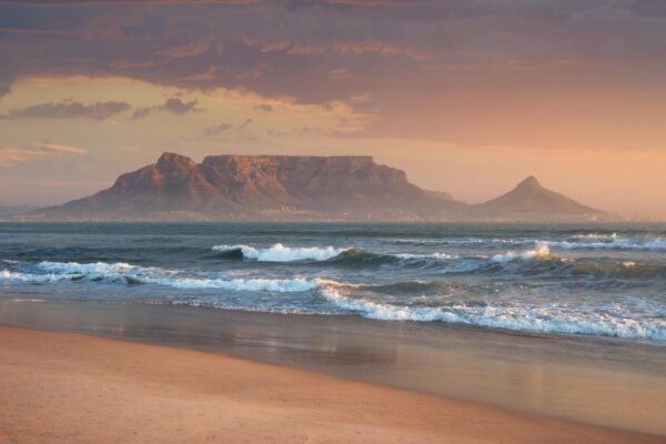 Rolling waves of Sunset Beach near Cape Town with a view of Table Mountain in the background at dusk
