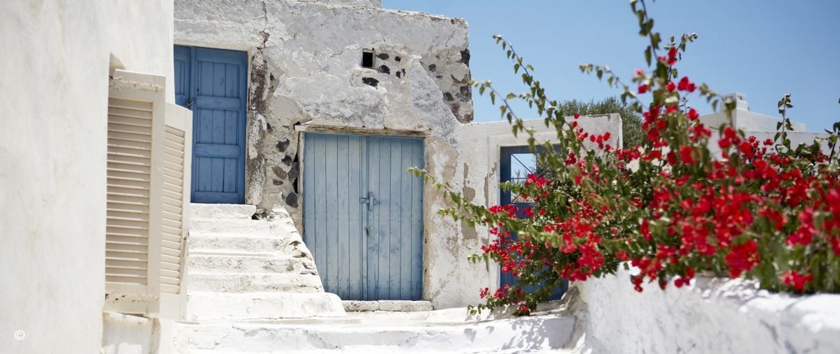 Red bouganvellia set against whitewashed stone building with blue wooden doors