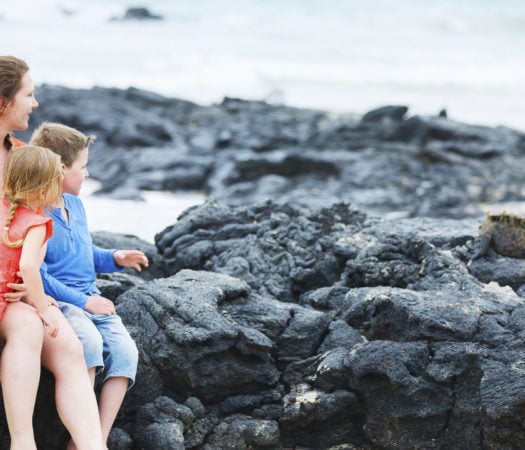 A family sit by as a marine iguana relaxes on a nearby rock